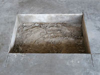 Creating the hole in the garage slab floor during the wall anchor installation in Highland.
